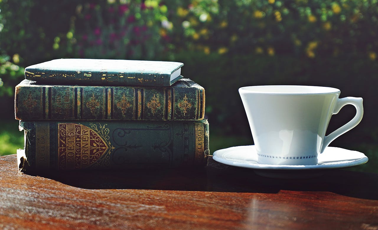 A tranquil setting with vintage books and a tea cup on a wooden table outdoors.